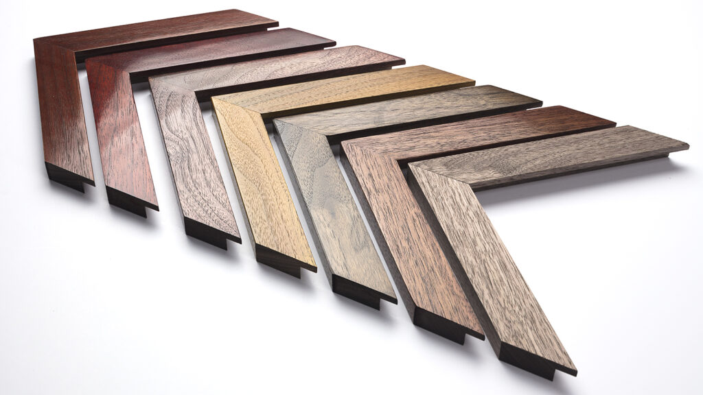 Eight wooden picture frame corners in various wood finishes are arranged in a zigzag pattern on a white surface, showcasing versatile styles that could complement anything from a floating frame for canvas to an elegant football shirt frame.