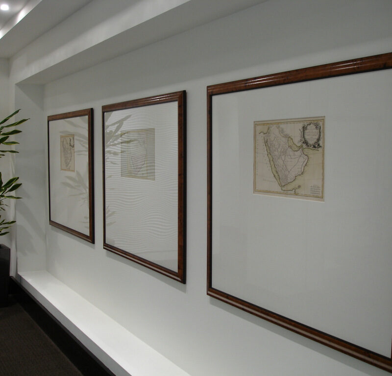 Three framed vintage maps hang on a white wall, much like how a football shirt frame might proudly display cherished memories. A potted plant is on the left side, and the ceiling features recessed lighting, casting a warm glow over the scene.
