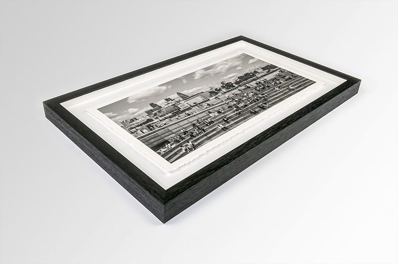 A sleek circle frame beautifully encases a matted black-and-white photograph, capturing a cityscape alive with people from an intriguing angle.