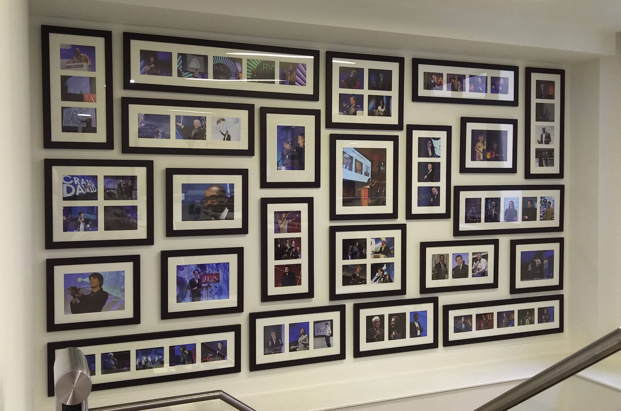 A wall display featuring multiple framed photos arranged in a grid, capturing various scenes and events on an office landing.