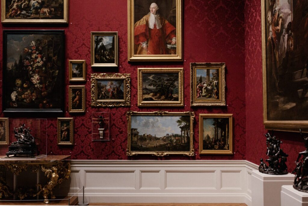 Multiple paintings framed on a red gallery wall