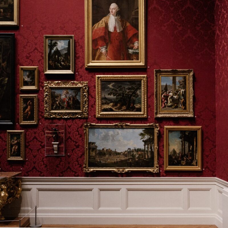 Multiple paintings framed on a red gallery wall