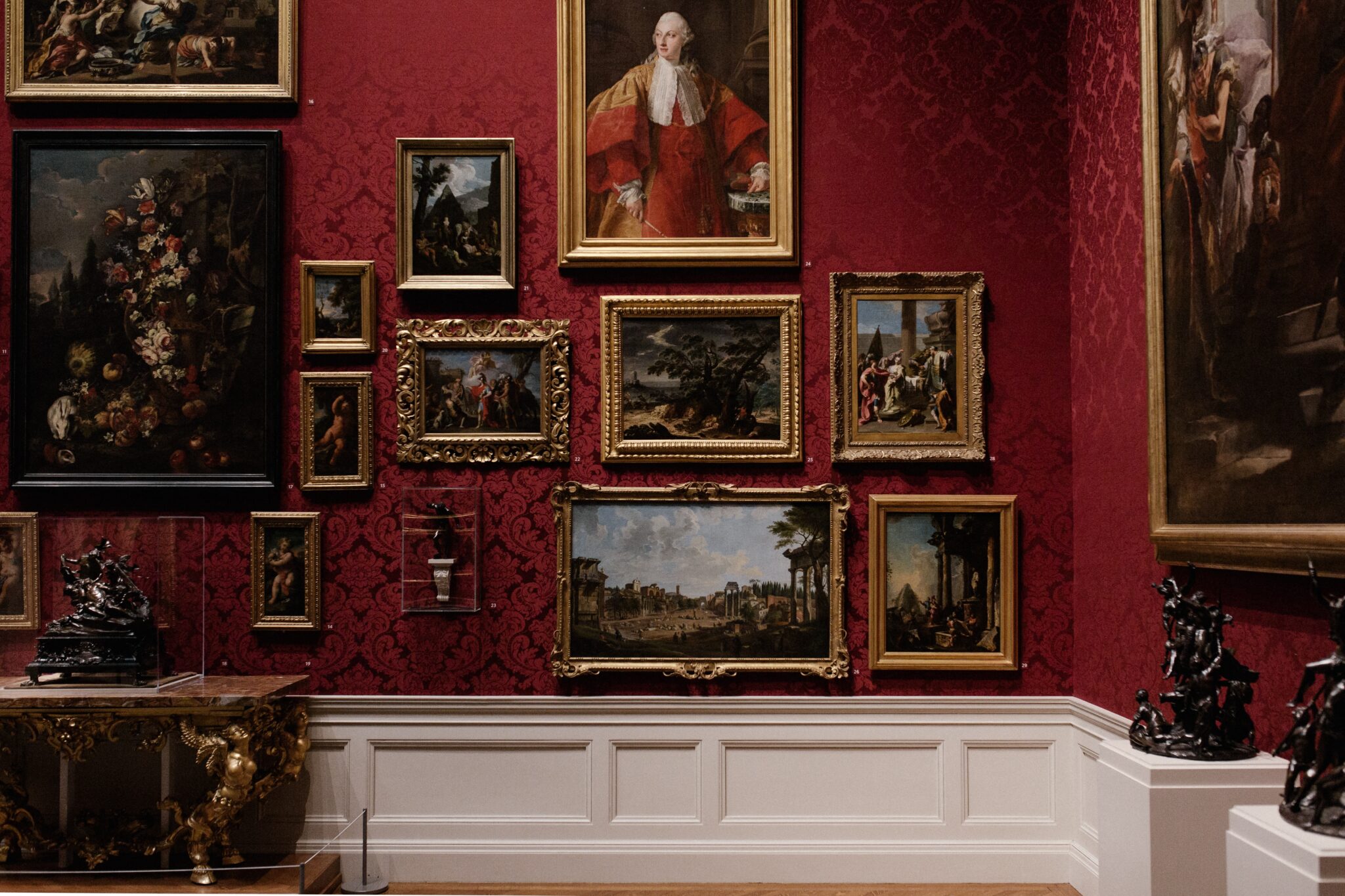 Multiple paintings framed on a red gallery wall