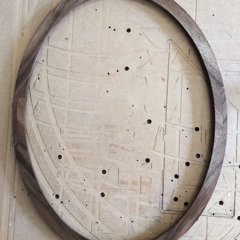 A wooden oval frame rests on a perforated, marked work surface.