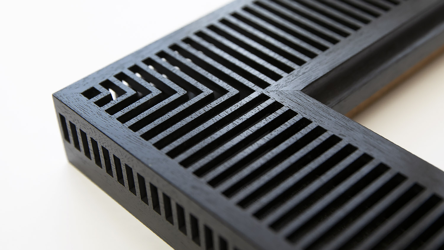 Close-up of a black, rectangular vent cover with geometric slotted patterns and right-angle corner.