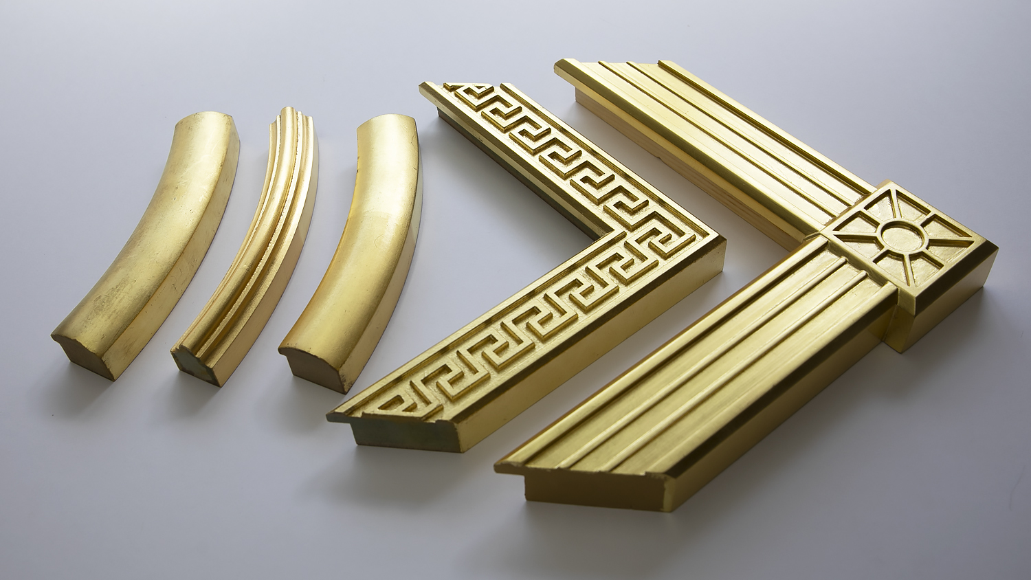 Four gold picture frame corners in different shapes and decorative patterns on a white surface.