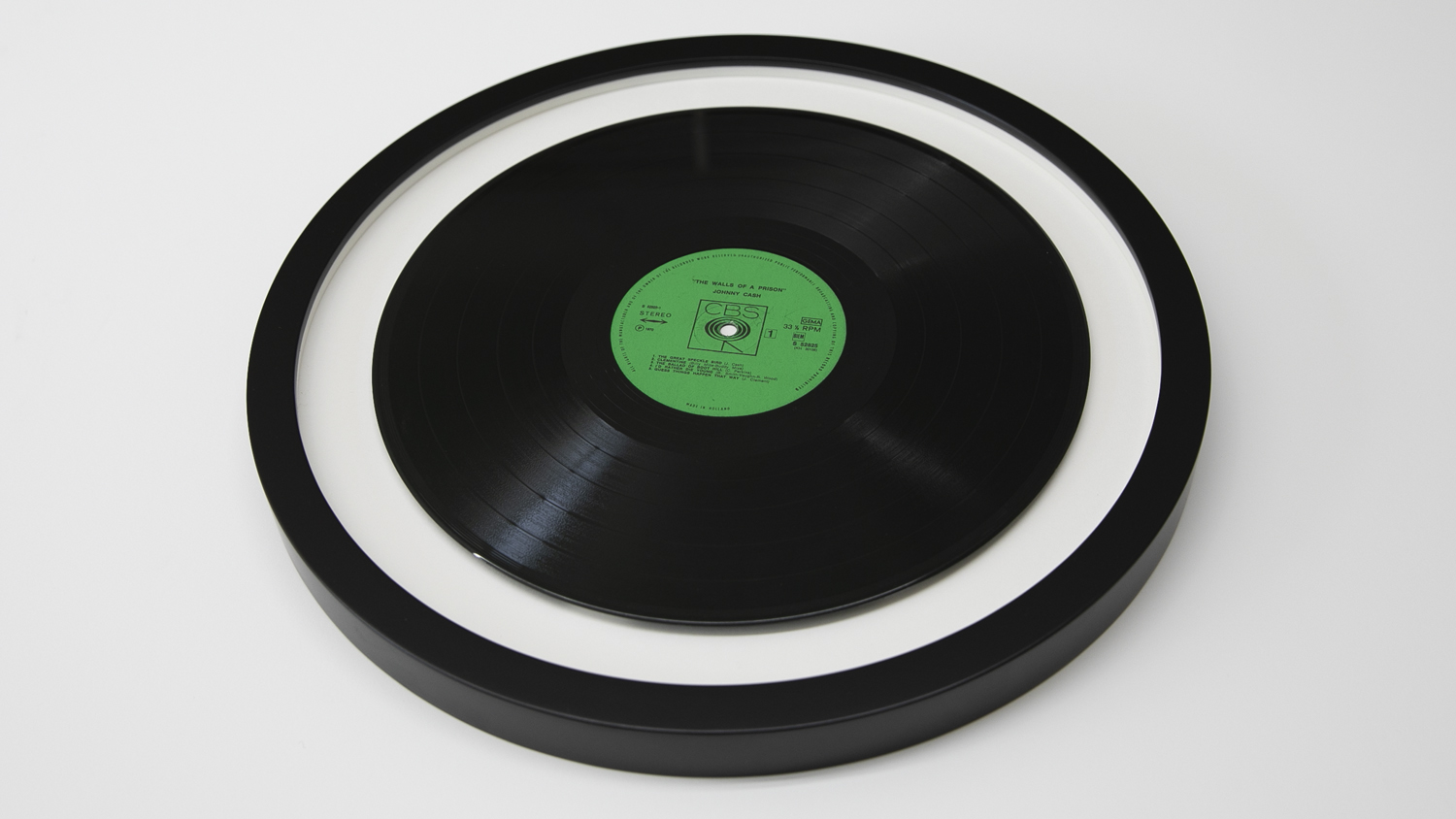 A black vinyl record is Vinyl Record Framing mounted in a round frame on a white background.