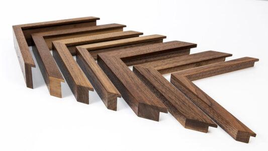 Seven wooden picture frame corners in different finishes are arranged in a row on a white surface.