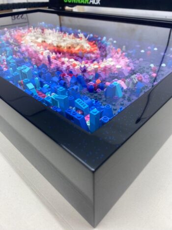 Framed 3D LEGO art depicting a colorful, abstract landscape with various blue and pink pieces.