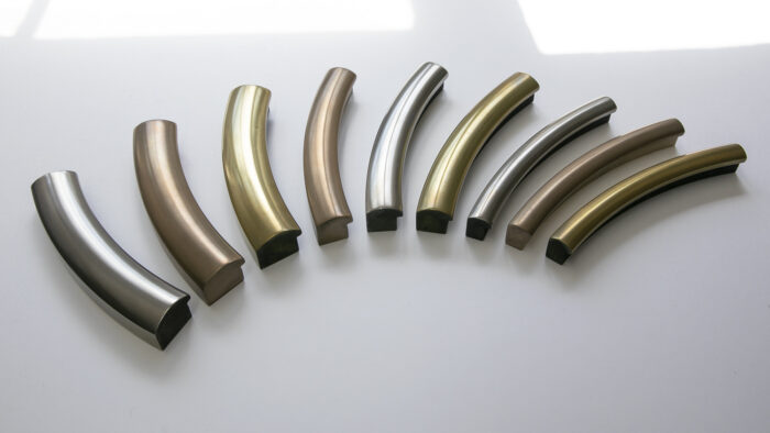Eight curved liquid metal frame tubes in various finishes, arranged on a white surface.