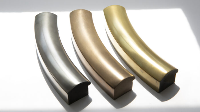Three curved gold liquid metal frame bars in silver, bronze, and gold rest side by side on white.
