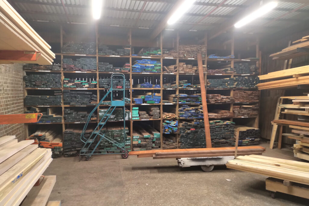 Stacks of assorted timber and lumber neatly organized on shelves in a warehouse with bright lighting.