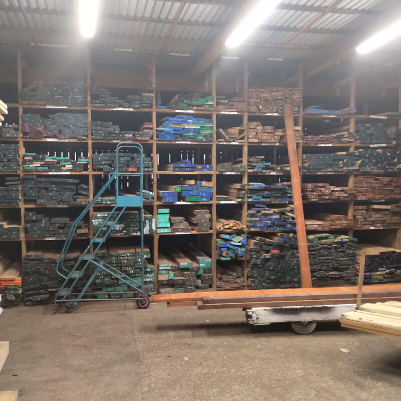 Stacks of assorted timber and lumber neatly organized on shelves in a warehouse with bright lighting.