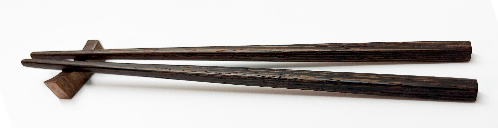A pair of dark wooden chopsticks rests on a matching wooden chopstick holder against a white background.