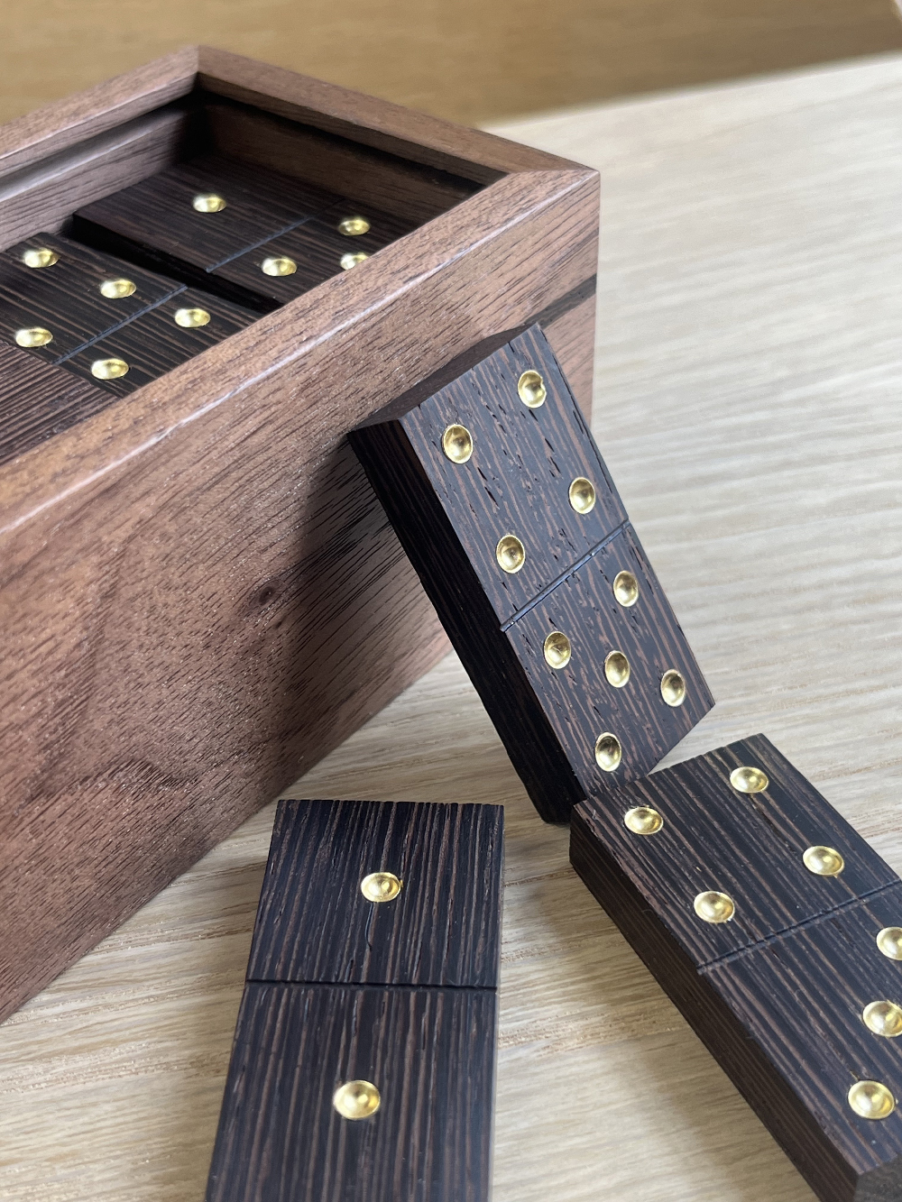 A wooden box with black dominoes, some inside and some resting on the edge and table.