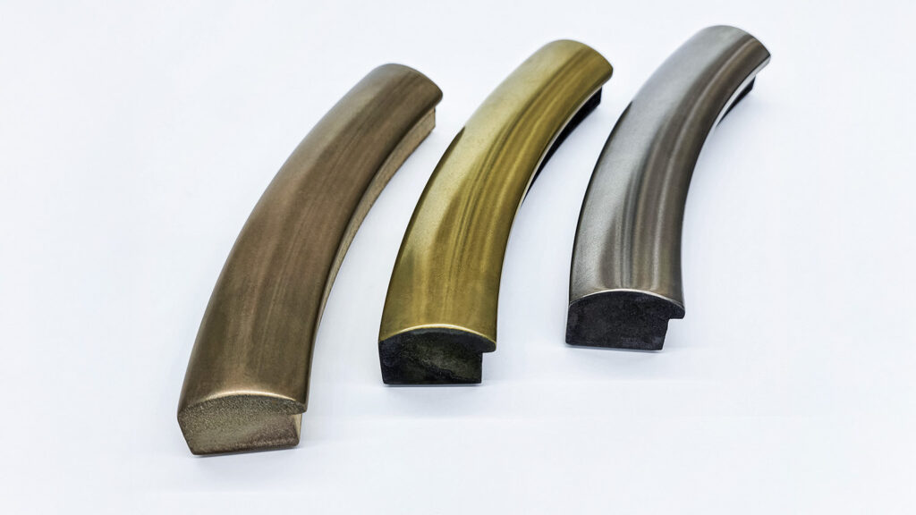 Three curved metal handles in bronze, brass, and nickel finishes on a white background.