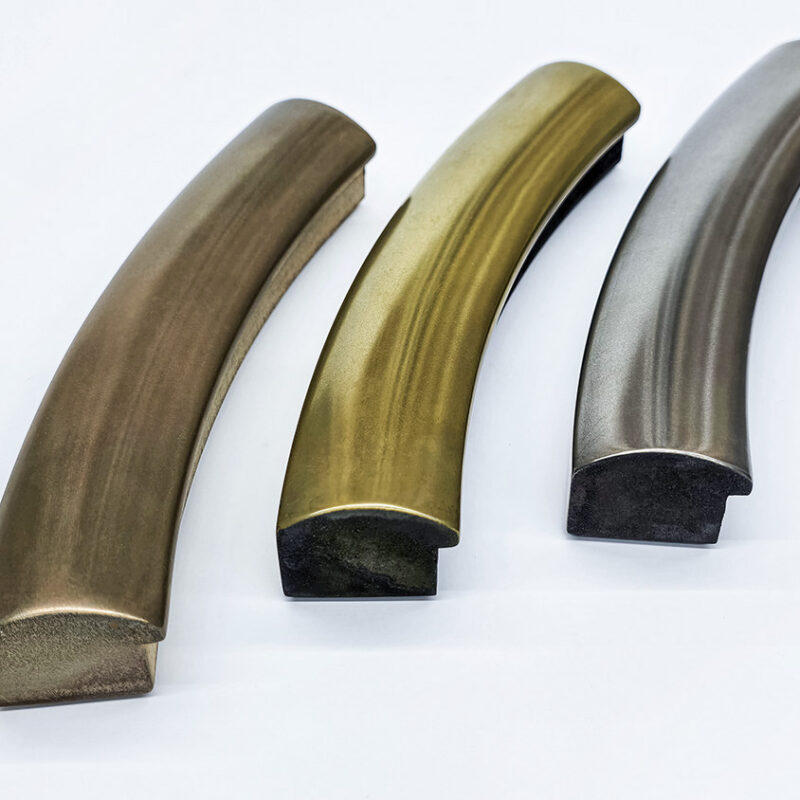 Three curved metal handles in bronze, brass, and nickel finishes on a white background.