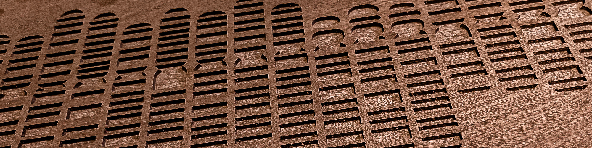 Close-up of a coppery-coloured Sapelie wood panel with rectangular and rounded cutout shapes in a patterned design to represent chromosomes.