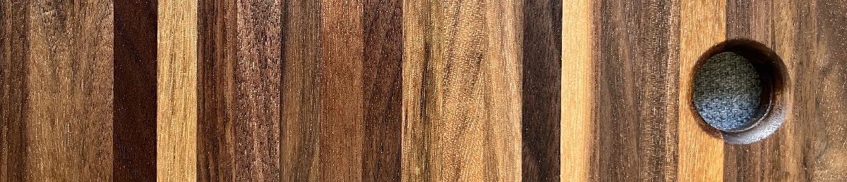 Close-up of a polished walnut wood chopping board made of vertical multicolored strips and a round hole on the right side.