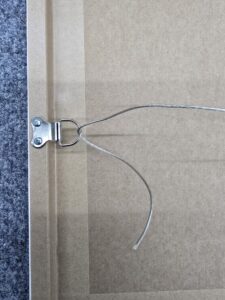 Close-up of a picture frame back with hanging wire threaded through a metal D-ring hanger.