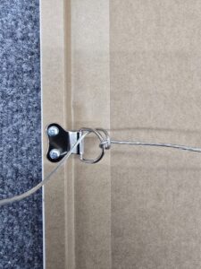 Close-up of a metal picture hanging wire attached to the back of a frame next to a carpeted floor.