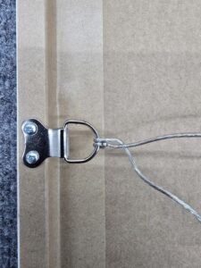 Close-up of a metal picture wire hanger attached to the back of a frame with two screws.