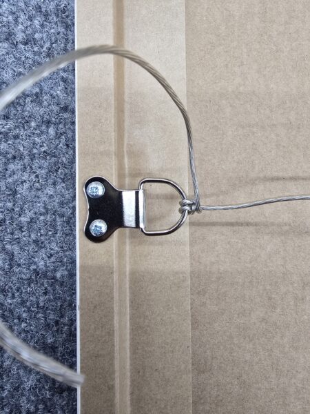 Close-up of a metal picture hanging wire screwed into the back of a frame on a carpeted surface.
