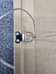 Close-up of a metal picture hanging wire screwed into the back of a frame on a carpeted surface.