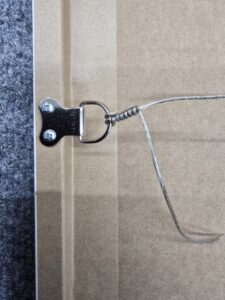 Close-up of a picture frame wire attached to a metal D-ring hanger on a cardboard backing.