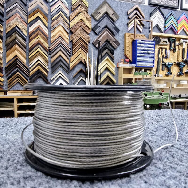 A spool of wire sits on a counter in a workshop with picture frames and tools on the wall.