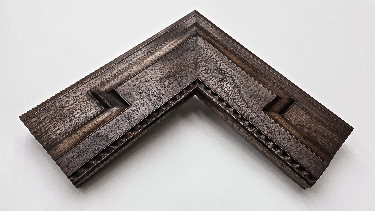 A picture frame corner in solid walnut in rich mahogany colour with a beadd inner rim and a bevelled front face. On a white background.