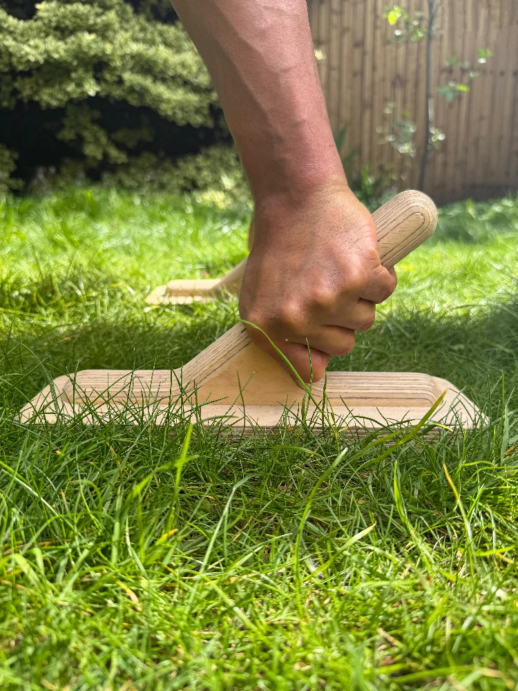 Close-up of a pair of planche parallettes on grass with a hand gripping the handles