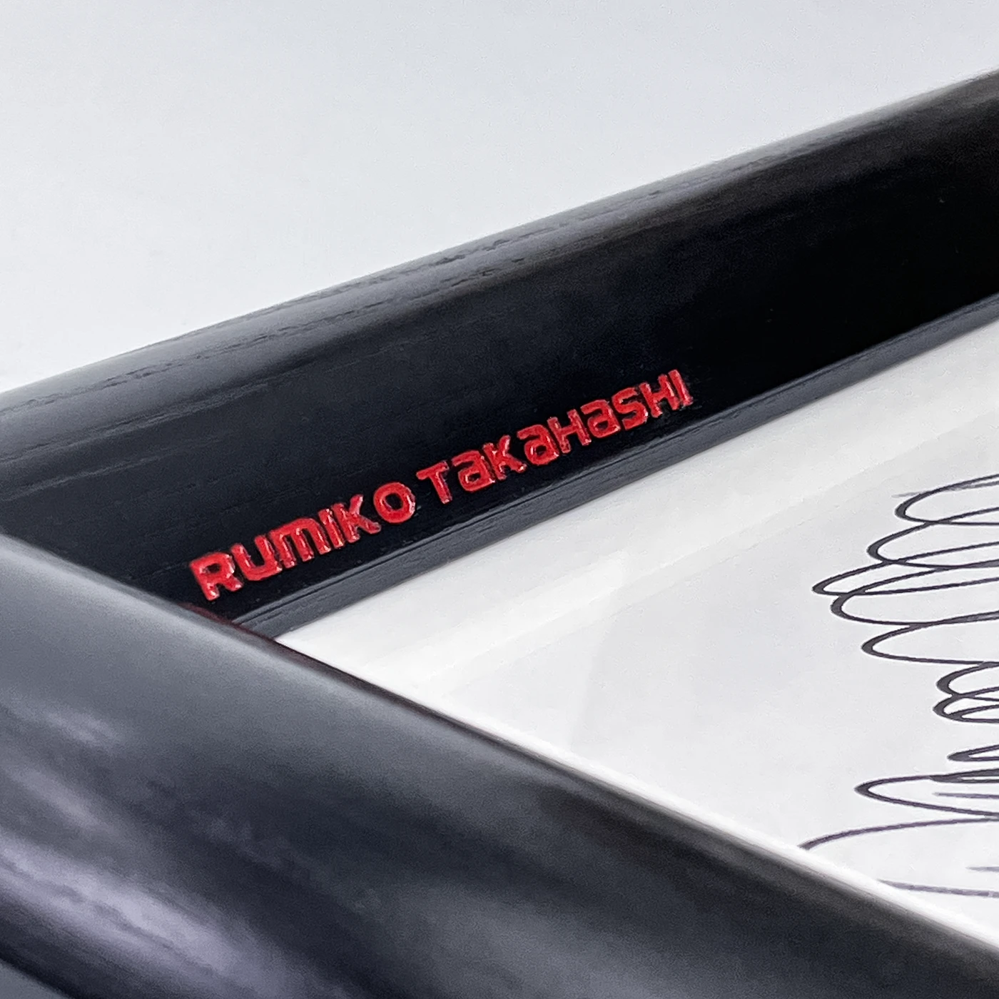 Close-up of wood engraving with the text carved into the inner sloping edge of a black wooden picture frame. The text is filled with red enamel paint.
