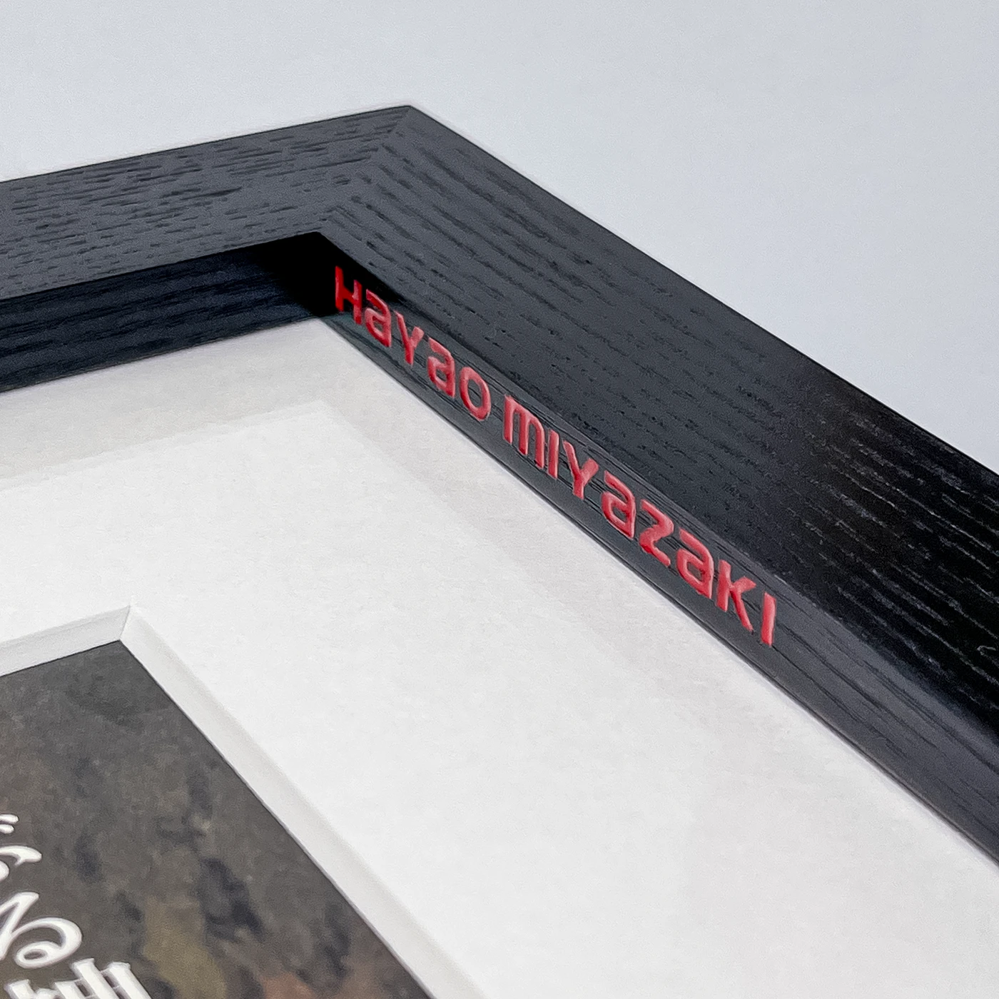 Close-up of wood engraving showcasing text on the sight edge of a black wooden picture frame. The text is filled with red enamel paint.