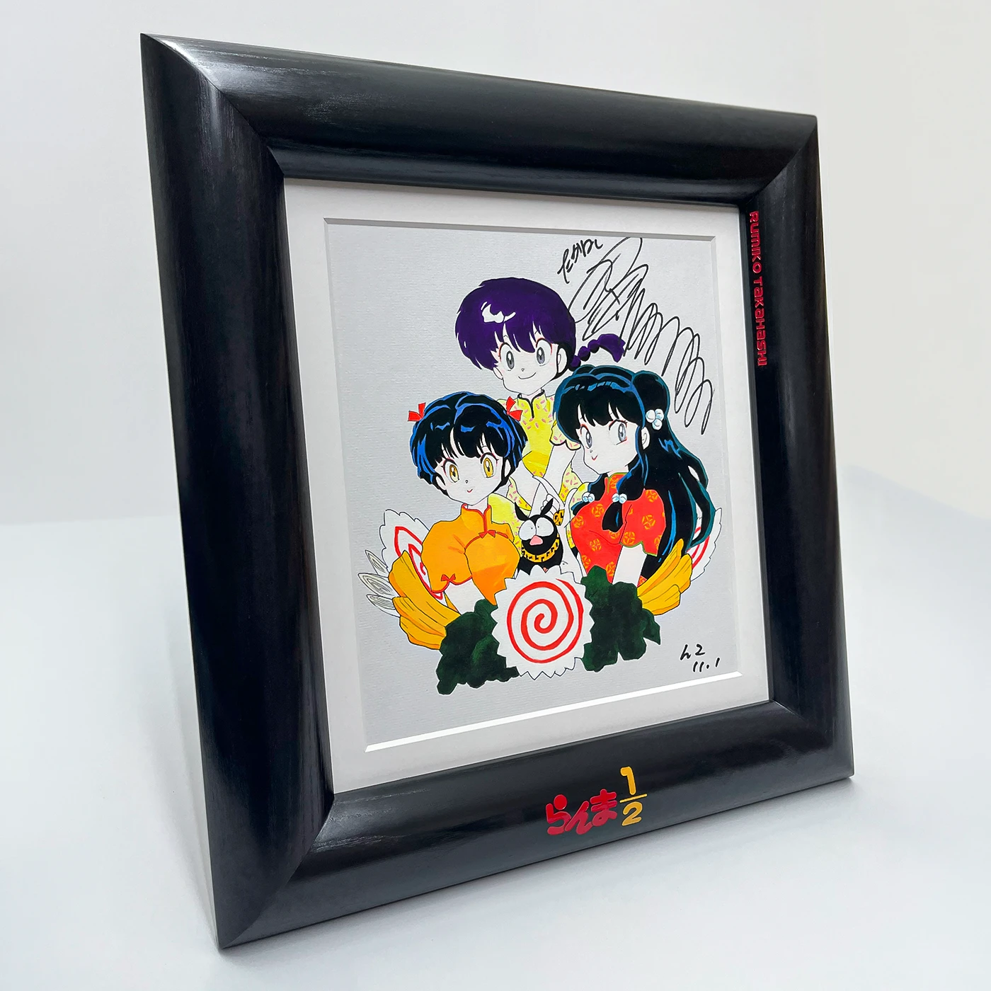 A square shaped black wooden picture frame with wood engraving on the front face and inner edge. The text is filled with yellow-orange and red enamel paint.