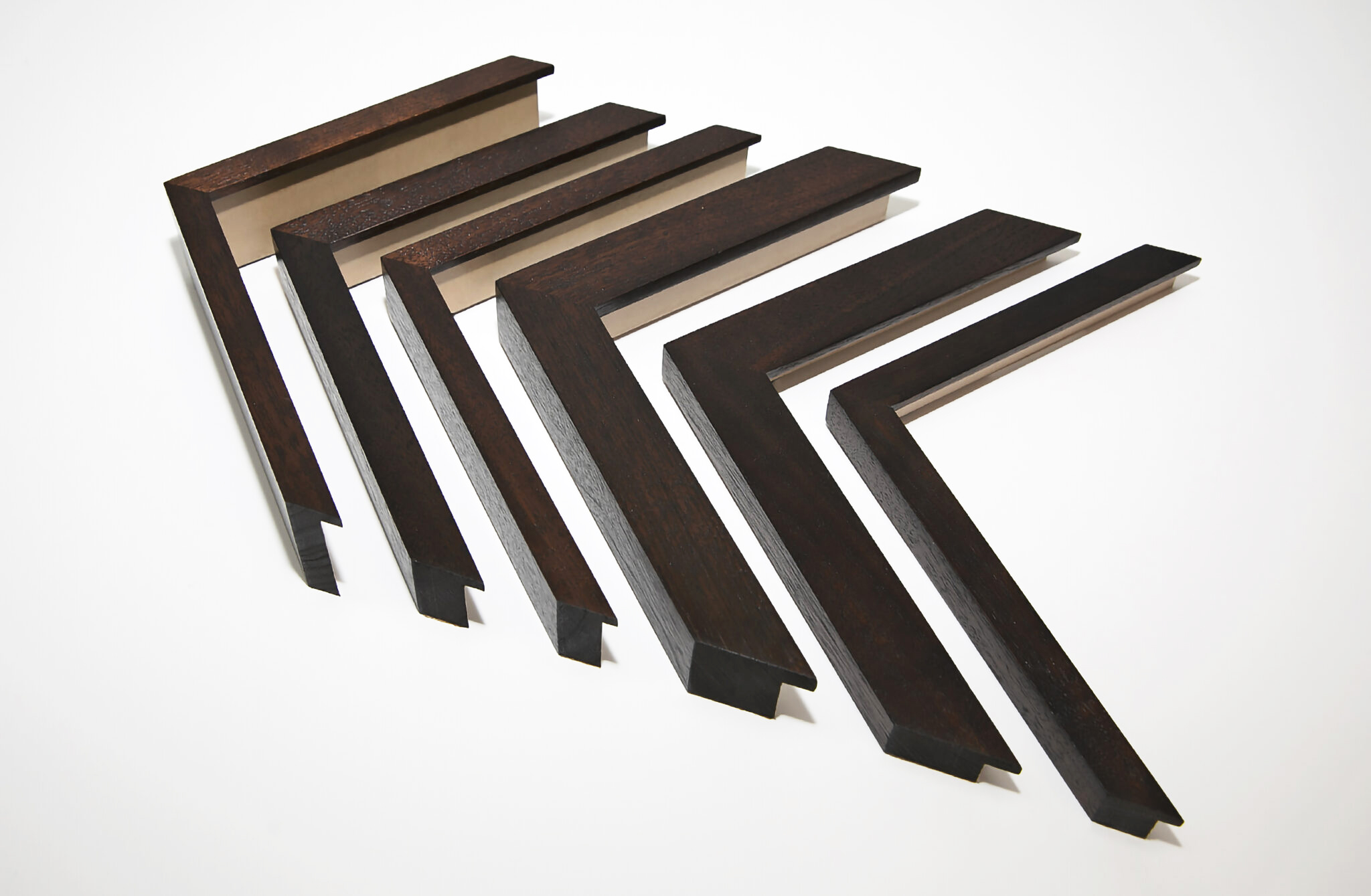 Six hand-finished picture frame corners in dark mahogany wood of various profiles sizes on a white background.