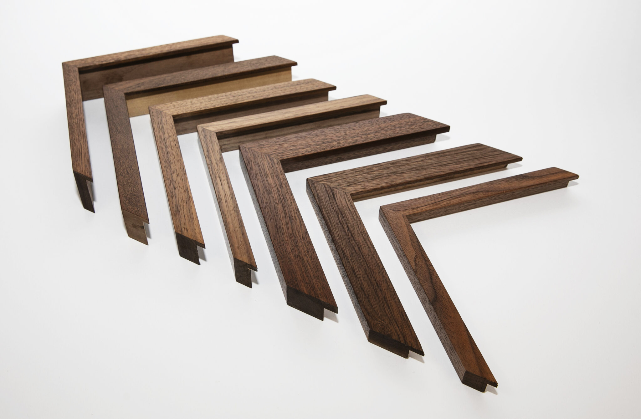 Seven hand-finished picture frame corners made from natural walnut wood on a white background