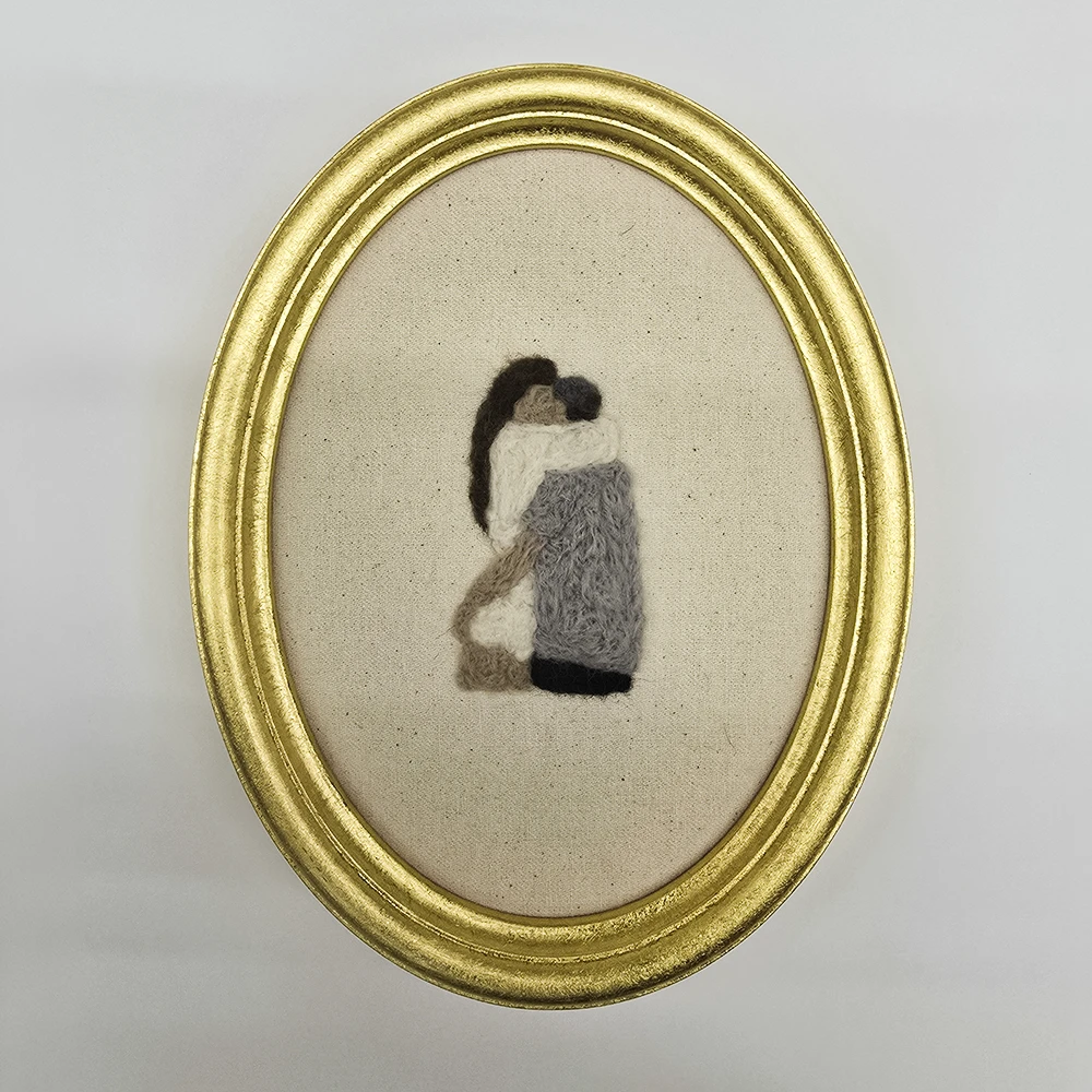 An embroidery showing a couple hugging framed in an oval frame in 22k gold leaf
